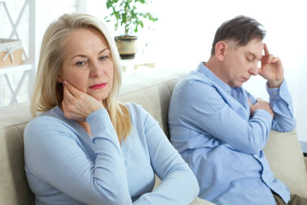Middle-aged couple sitting apart on a couch, both looking stressed and distant