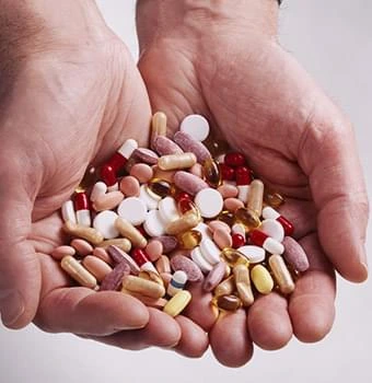 Hands holding a large handful of mixed pills and capsules